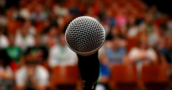 Image of a microphone, facing a full audience