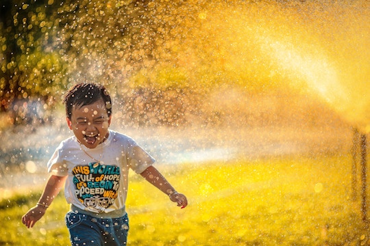Image of a small boy running through sunlighted sprinkler