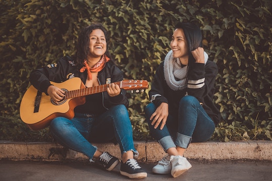 Image of two women playing guitar and singing while sitting on a curb