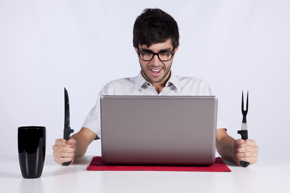 Image of a man at a computer with a knife and fork in his hands