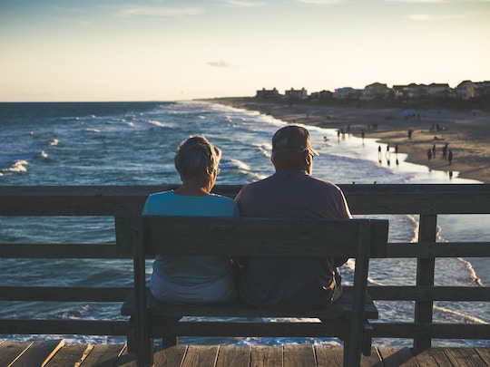 Image of an older couple sitting on a bench overlooking the ocean