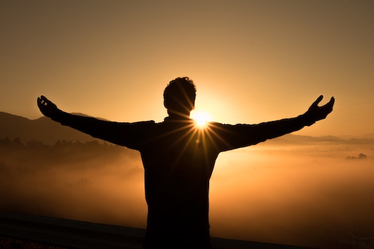 Image of a man facing the sunrise with arms outstretched
